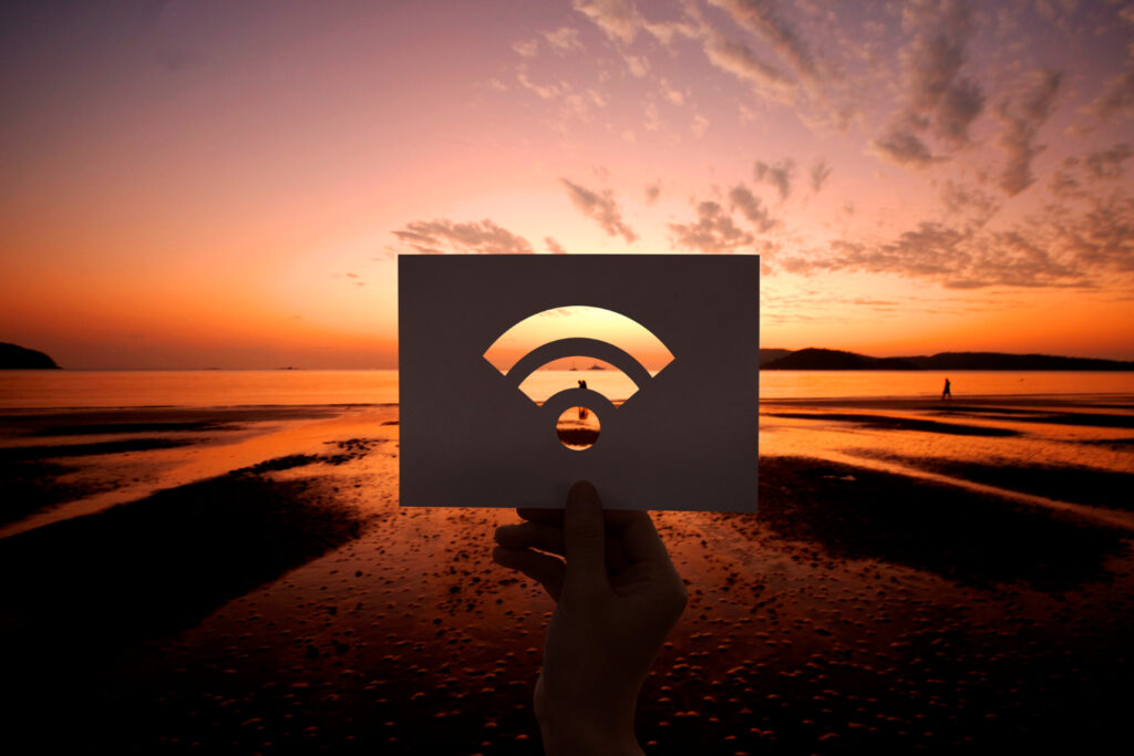 Nell'immagine una mano tiene un cartocino con il simbolo del wi-fi sullo sfodo di uno splendido tramonto sul mare - Smart Marketing