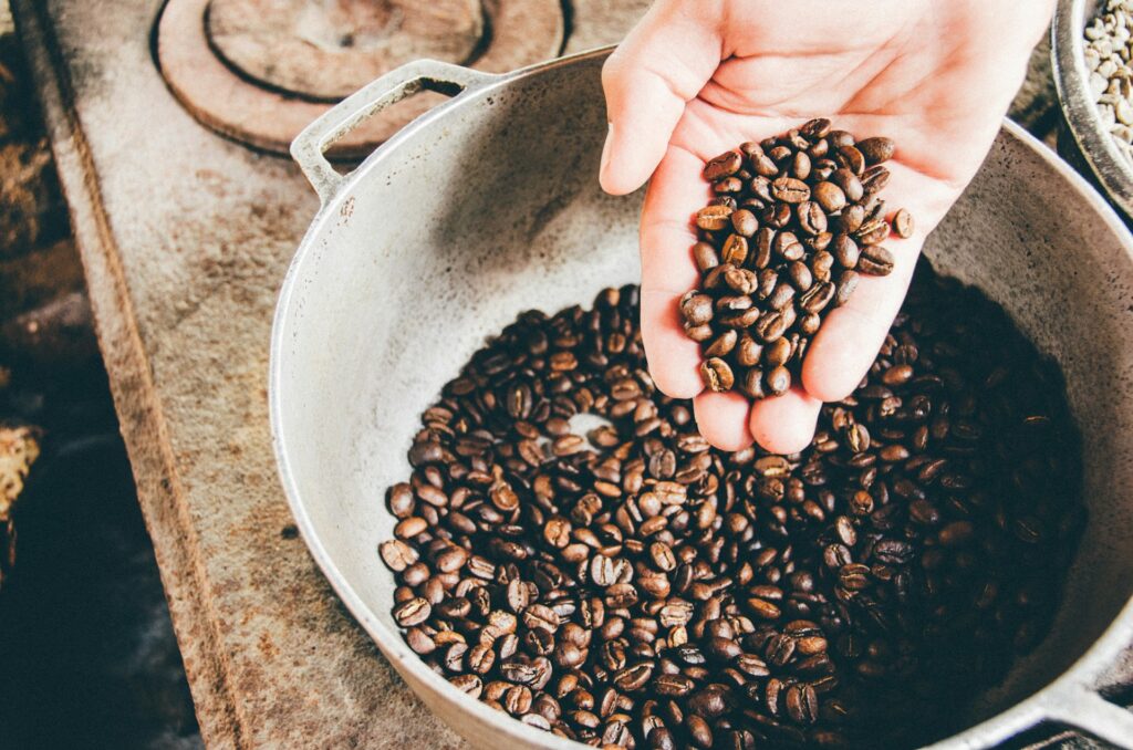 Nell'immagine una mano raccoglie dei chicchi di caffe da una pentola di acciaio - Smart Marketing